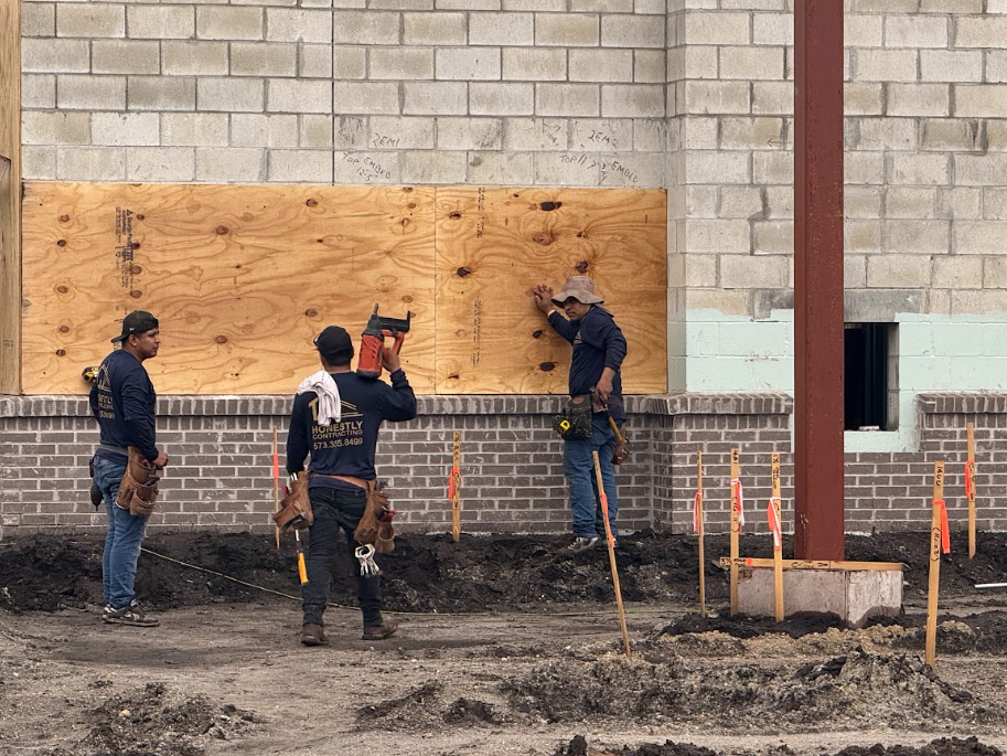 Crew boarding up an exterior wall of a commercial building ahead of storm protection
